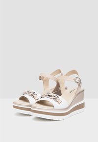 Wedge sandals with a white leather upper, beige accents, silver chain detail, and adjustable ankle strap on a multi-toned platform sole.