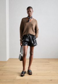 Bruine, fuzzy trui met V-hals, gecombineerd met zwarte neplederen shorts met een riem. Zwarte block-heeled sandalen en een kleine handtas.