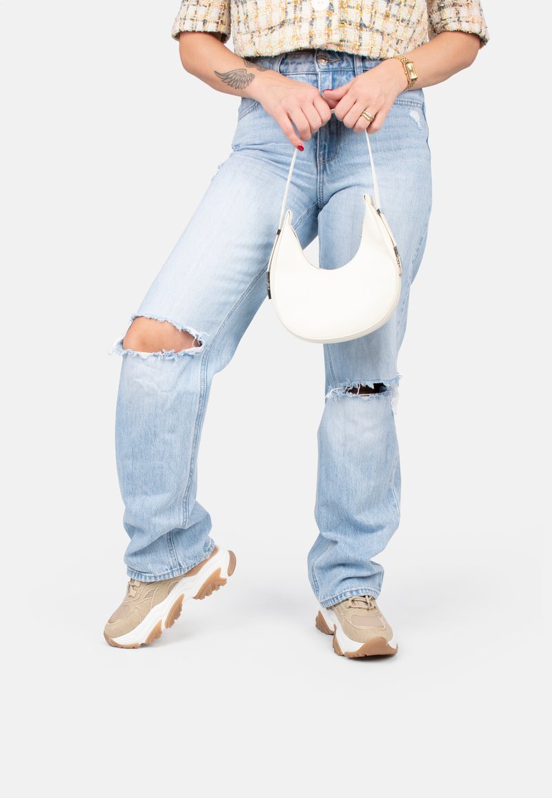 Sac à main blanc, courbé, tenu à la main, associé à un jean bleu clair déchiré avec des trous aux genoux et des baskets beiges à semelles épaisses.