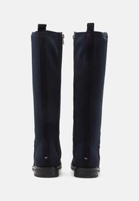 Mörkblå knähöga stövlar med en ribbad textilöverdel, mockadetaljer, sidodragkedjor och en platt gummisula. Logotags vid hälen.
