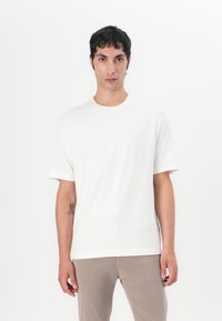 Tricou alb cu mânecă scurtă, cu o suprafață texturată, guler rotund și croială lejeră, asortat cu pantaloni khaki deschis.