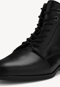 Bottine en cuir noir avec une finition lisse, bout rond et semelle plate. Présente des lacets noirs et des œillets en métal, soulignant un design épuré.