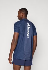 Marineblå treningstrøye med melert stoff, med et stort hvitt "ellesse"-logo på ryggen og korte ermer, kombinert med shorts.