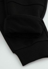 Czarne sportowe spodnie z teksturowanej tkaniny, z mankietami na końcach i prążkowanymi akcentami. Widoczna gładka powierzchnia i przeszycia.