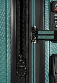 Valigia rigida di colore teal con una finitura testurizzata. Caratterizzata da una doppia zip, dettagli neri e un meccanismo di serratura a combinazione.