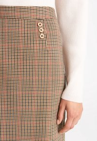 Hnědá károvaná sukně s kostkovaným vzorem s červenými akcenty a třemi ozdobnými dřevěnými knoflíky na pasu.