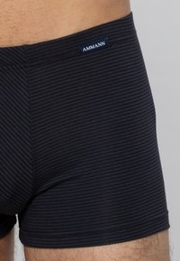 Mäns mörkblå randiga boxershorts, tillverkade av mjukt tyg. Har en logotags på midjebandet och en slät yta. Visad ur ett vinkel av övre låret.
