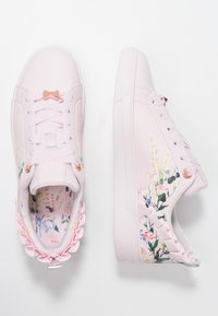 Baskets rose pâle avec imprimé floral sur les côtés, éléments brillants en or rose, lacets texturés et détails froncés au niveau du talon.