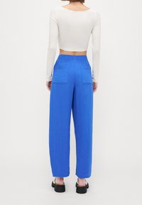 Blå vida byxor i en texturerad kvalitet, med två bakfickor och elastisk midja. Matchas med en vit långärmad crop top.