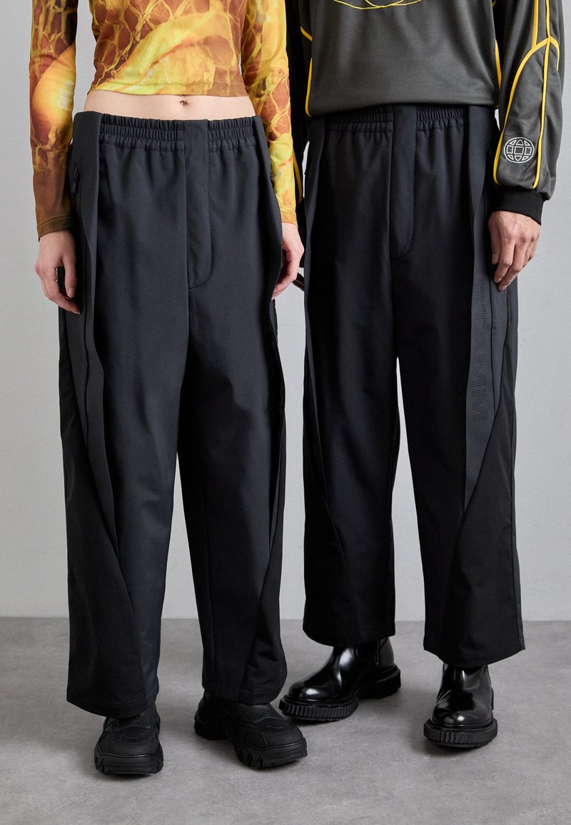 Czarne spodnie szerokie z gładkim wykończeniem, z bocznymi kieszeniami na zamek błyskawiczny i kontrastowymi panelami w lekkim materiale.