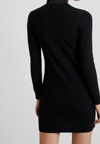 Robe noire en maille avec manches longues, coupe ajustée et col texturé. Design simple sans motifs ni accents.