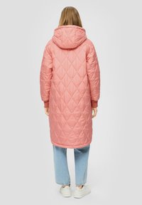 Langer rosa gesteppter Mantel mit Kapuze, versehen mit Rautenmustern, elastischen Bündchen und einer Länge bis zur Mitte der Oberschenkel, kombiniert mit hellblauen Jeans und Sneakers.