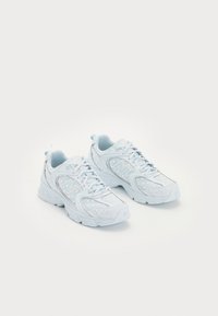 Vaaleansiniset urheilukengät, jotka on valmistettu synteettisestä materiaalista ja joissa on pehmustettu nilkkareuna, rei'itettyjä yksityiskohtia sekä heijastava logo sivulla.