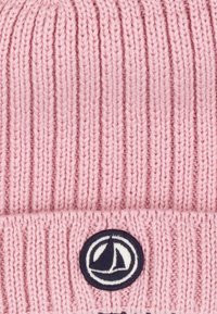 Beanie rosa lavorato a maglia con texture a costine e bordo piegato. Presenta una toppa rotonda blu navy con un design di veliero sul davanti.