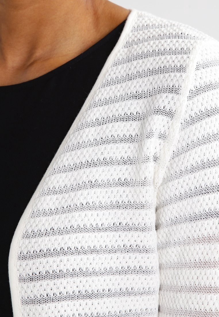 Cardigan bianco a maglia con strisce orizzontali a traforo, morbido al tatto e dalla vestibilità rilassata, indossato su un top nero.