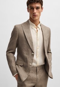 Light brown linen suit with a tailored fit, featuring a two-button closure, notch lapels, and a cream button-up shirt underneath.