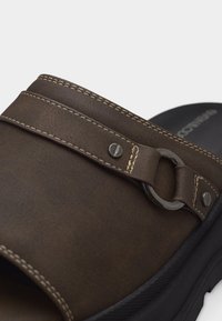 Καφέ δερμάτινο σανδάλι slide με ασημένια λεπτομέρεια δαχτυλιδιού και ορατή ραφή στη μαύρη σόλα, πάνω σε ανοιχτό φόντο.