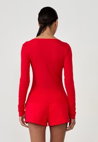 Czerwony, żebrowany top z długim rękawem o szerokim dekolcie, zestawiony z pasującymi czerwonymi szortami. Gładka tekstura i dopasowany krój.