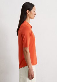Korte mouwen polo shirt in oranje stof met een klassieke kraag, gladde textuur en een relaxte pasvorm, gecombineerd met lichtgekleurde shorts.