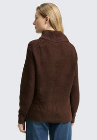 Brauner Strickpullover mit hohem Kragen, gerippter Textur und tailliertem Saum. Die Rückseite zeigt ein detailliertes Strickmuster und hat lange Ärmel.