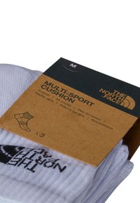 Calcetines blancos de longitud trimestral con tejido texturizado y logo negro. Incluyen empaquetado en colores marrón y verde oscuro, etiquetado como "Multi-Sport Cushion."
