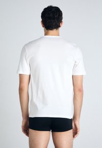 T-shirt en coton blanc à manches courtes, col rond et texture lisse, porté avec un short noir ajusté. Vue de dos.