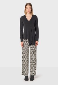 Svart långärmad topp med v-ringning, lagerdesign, kombinerad med byxor med vida ben som har ett krämfärgat geometriskt mönster och grå stövlar.