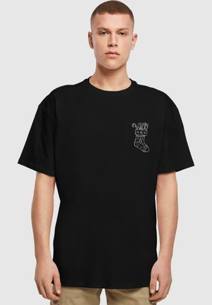 Black cotton t-shirt featuring a white graphic of a Christmas stocking with gifts and candy canes, short sleeves, and a relaxed fit.