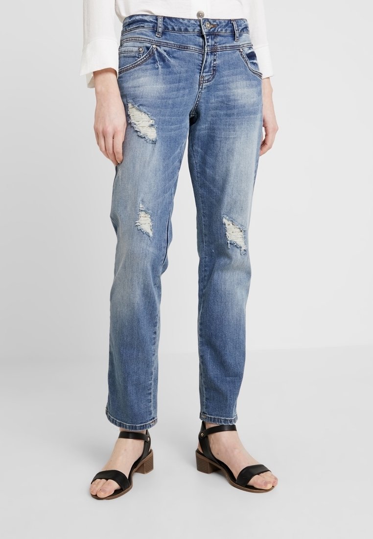 Ljusblå slitna denimjeans med rivningar på låren, klassisk femfickdesign, raka ben, som matchar med svarta sandaler med remmar.