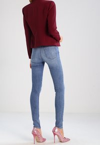 Blazer bordeaux sur mesure, jean skinny bleu clair, et talons hauts roses pailletés. Tissu lisse, coupe ajustée, et bouts pointus des chaussures.