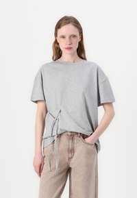 Gray cotton t-shirt with short sleeves, featuring a drawstring detail at the hem and a relaxed fit, paired with light beige jeans.