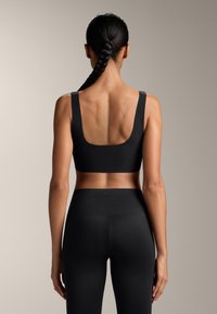 Czarny stanik sportowy z szerokimi ramiączkami i okrągłym tyłem, wykonany z gładkiego, elastycznego materiału. Połączony z czarnymi legginsami o wysokim stanie.