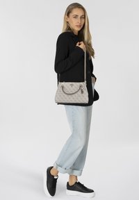 Geantă bej cu formă structurată, suprafa�ță cu model, două mâneruri și o curea detașabilă pentru umăr, asortată cu blugi cu tiv răsucit și adidași.
