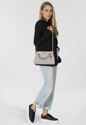 Sac à main beige à forme structurée, surface à motifs, double poignée et bandoulière amovible, associé à un jean retroussé et des baskets.