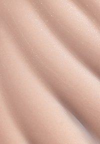 Gros plan d'échantillons de fond de teint liquide beige clair, lisses, avec un subtil éclat et une texture crémeuse.