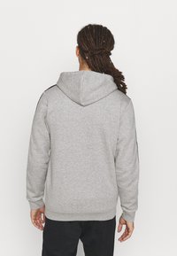 Sudadera con capucha gris, de manga larga y con dobladillo acanalado. Presenta detalles negros en los hombros y un tejido suave y texturizado.