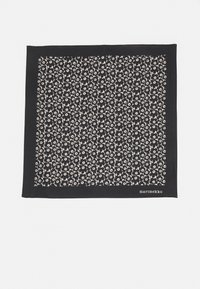 Écharpe noire à motif, ornée d'un design floral blanc, en tissu doux, de forme carrée avec un détail de marque dans le coin.