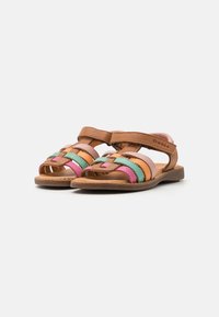 Sandalias de cuero marrón con tiras tejidas multicolores en rosa, verde y naranja. Suela plana y cierre ajustable de gancho y bucle.