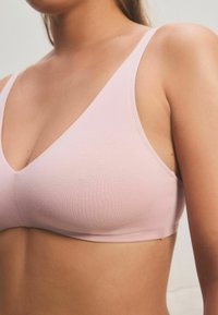 Bralette rosa chiaro con una texture morbida e liscia, caratterizzato da un design a scollatura a V e sottili spalline regolabili. Costruzione senza cuciture per un comfort ottimale.