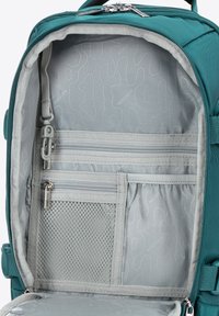 Wnętrze turkusowego plecaka ma jasnoszare wykończenie z falistym wzorem, liczne kieszenie na zamek oraz siatkową przegrodę do organizacji.