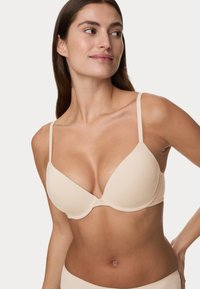 Reggiseno imbottito beige con spalline regolabili, texture liscia e design senza cuciture. Presenta una forma triangolare classica e una chiusura a gancio e asola.