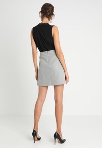 Un haut sans manches noir associé à une mini-jupe grise. La jupe a une coupe droite et une fermeture éclair à l'arrière. Des escarpins noirs viennent parfaire le look.