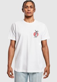 Tricou alb din bumbac cu un grafic de iepure de desene animate gri pe partea stângă a pieptului, conturat în roșu cu modele complexe.