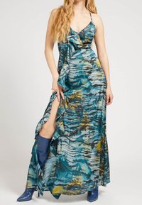 Robe maxi dans un imprimé abstrait bleu, turquoise et jaune. Présente un décolleté en V profond, des accents volantés et une fente haute. Associée à des bottes bleues.