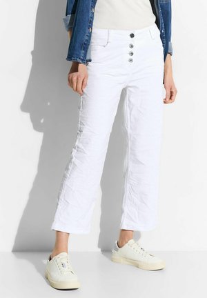 Pantalon blanc court taille haute avec quatre boutons sur le devant, associé à des baskets blanches, une veste en jean bleue et un haut blanc.