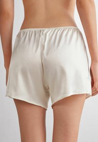 Satijnen beige shorts met een glanzende textuur, voorzien van een elastische tailleband en een losse pasvorm, die halverwege de dij eindigen met een omgestikte rand.