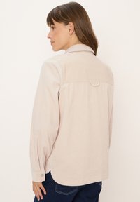 Lichtroze corduroy overhemd met knoopmanchetten en een rugpasdetail. Heeft verticale ribbels en een ronde zoom.