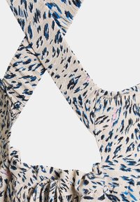 Kevyt kangas, jossa on beige tausta, johon on painettu sinisiä ja mustia abstrakteja kuvioita. Ristikkäiset hihnat ja kerrostettu yksityiskohta kaula-aukossa.