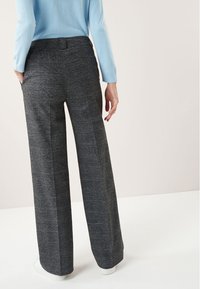 Pantalons larges en tissu texturé gris foncé, présentant un motif à carreaux subtil et une taille haute. La vue arrière met en valeur une coupe soignée.