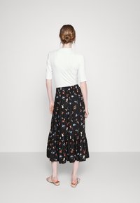 Saia preta com padrão floral apresentando flores vermelhas, azuis e amarelas. A saia tem uma bainha pregueada e é usada com uma blusa branca justa.